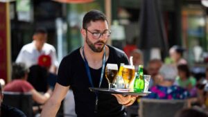 Camarero con contrato temporal sirviendo bebidas en terraza relacionado con la ayuda del SEPE de 570 euros