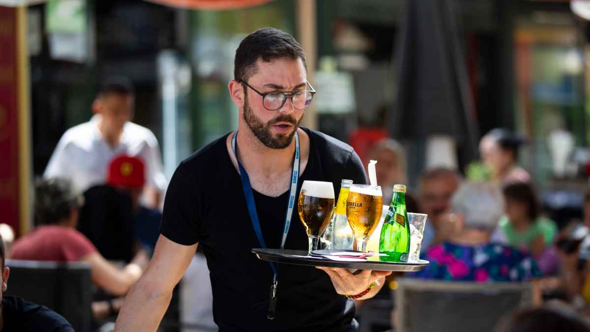 Camarero con contrato temporal sirviendo bebidas en terraza relacionado con la ayuda del SEPE de 570 euros