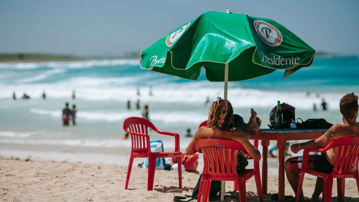 Personas sentadas bajo una sombrilla verde en la playa de República Dominicana