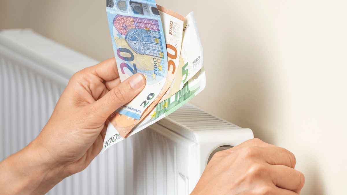 Persona ajustando la calefacción con billetes de euro sobre un radiador, ayuda del Bono Social Térmico 2025.