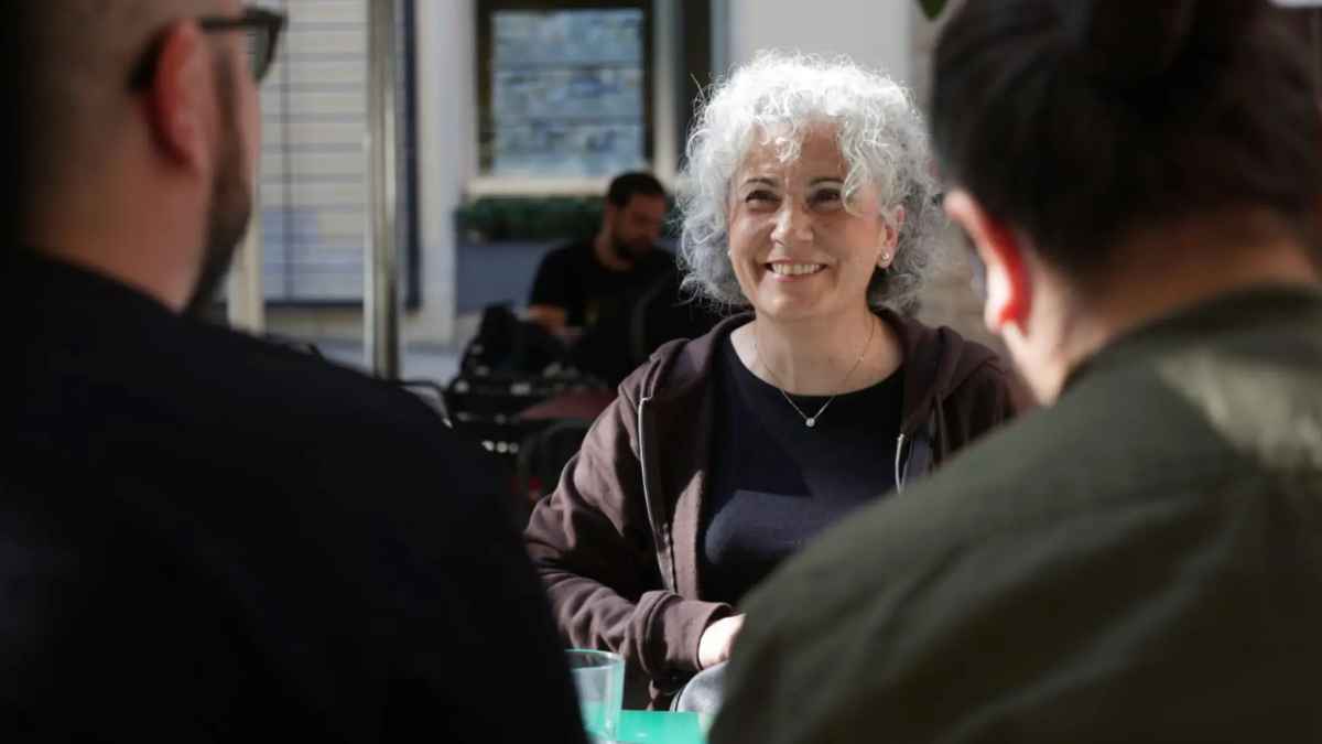 Mujer mayor sonriente hablando con otras personas, representación de los beneficiarios del subsidio y del Ingreso Mínimo Vital compatibles.