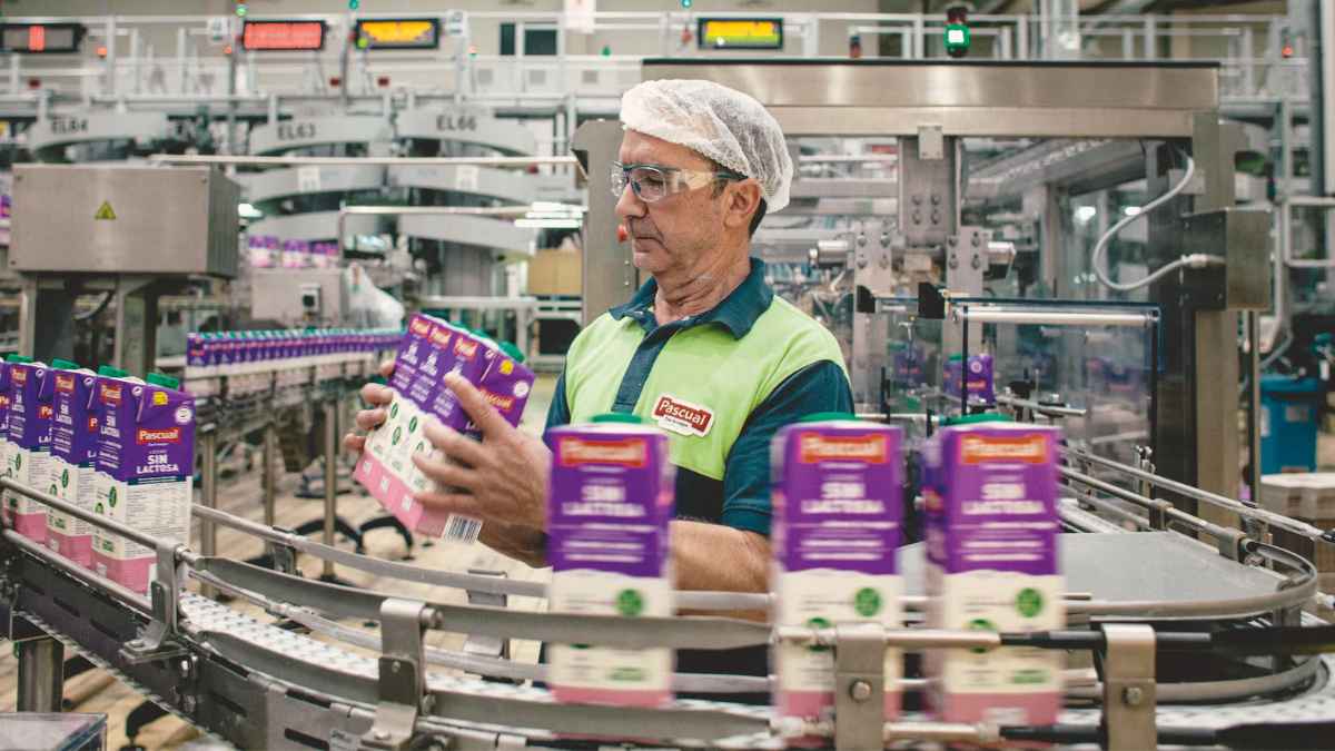 Trabajador en planta de producción de Pascual manipulando envases de leche en la línea de envasado