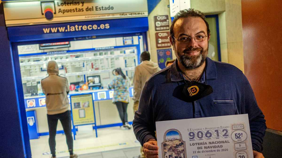 Lotero frente a administración de lotería en Almería mostrando un décimo de Navidad
