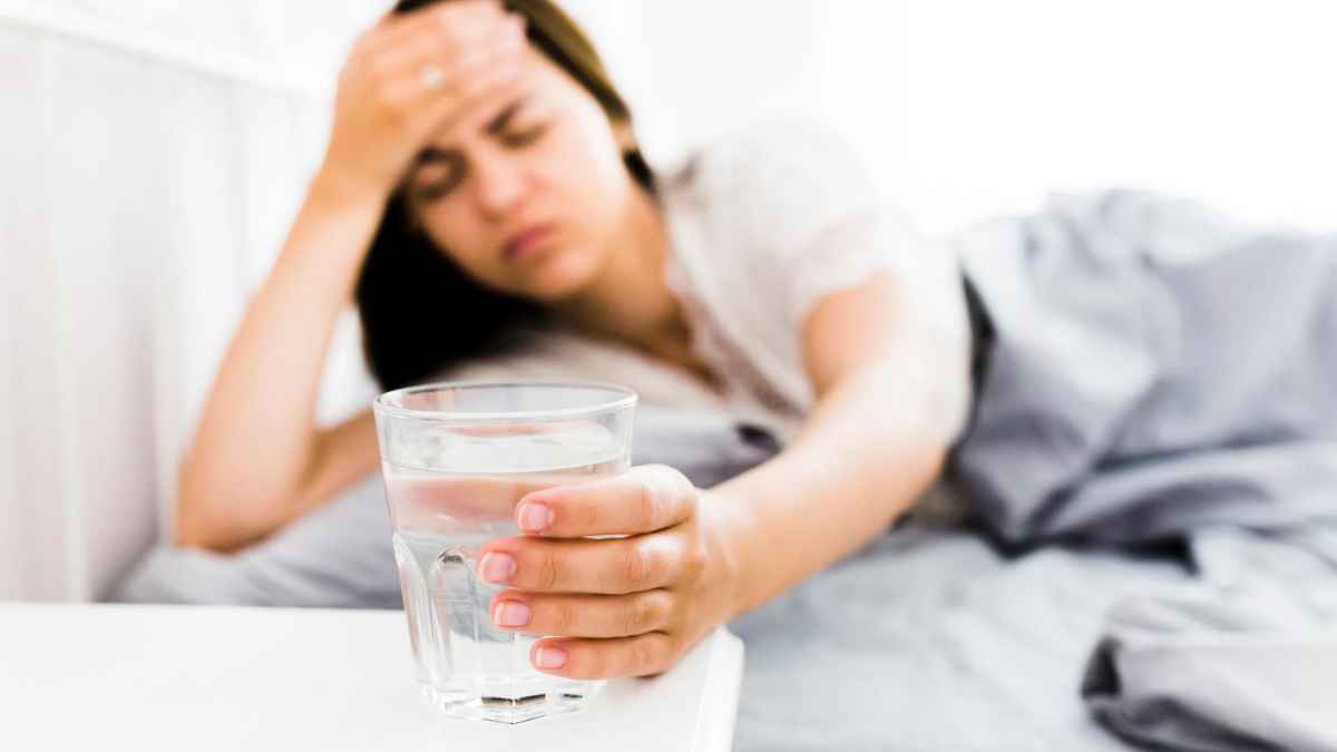 Mujer con dolor de cabeza sosteniendo un vaso de agua por una migraña