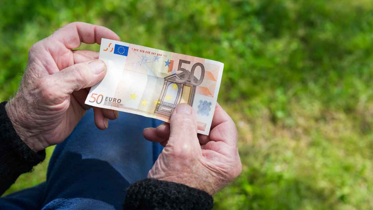 Manos de una persona mayor sujetando un billete de 50 euros relacionado con la pensión no contributiva.