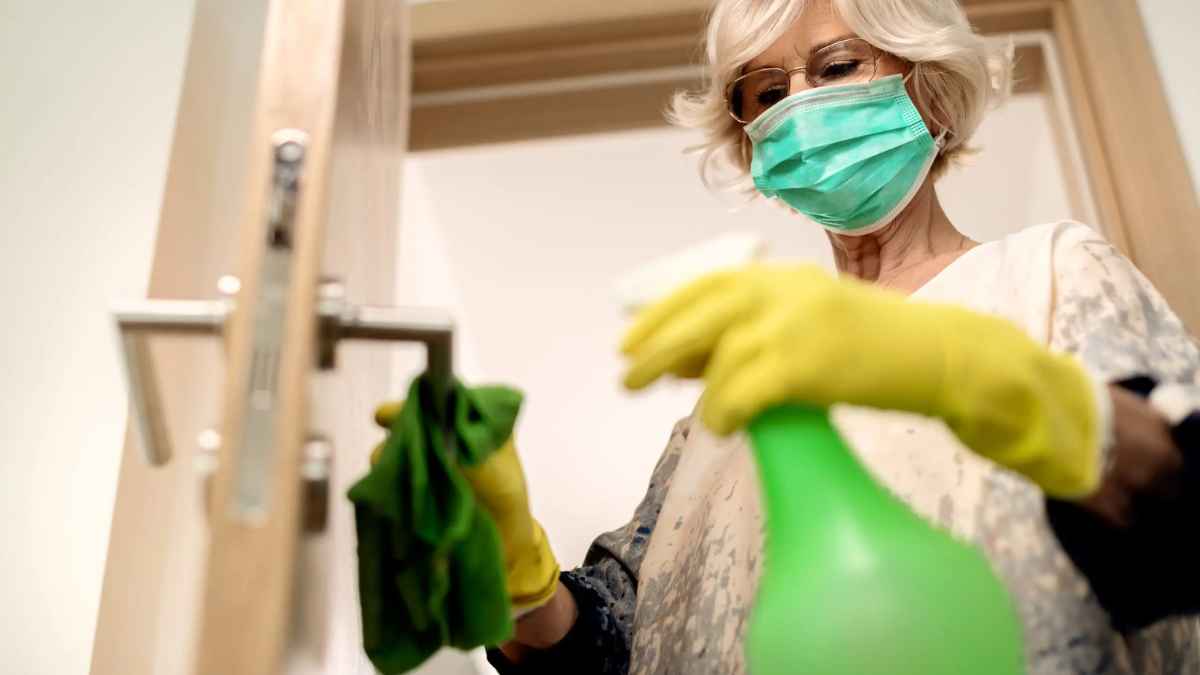 Trabajadora realizando tareas de limpieza con guantes y mascarilla en una puerta