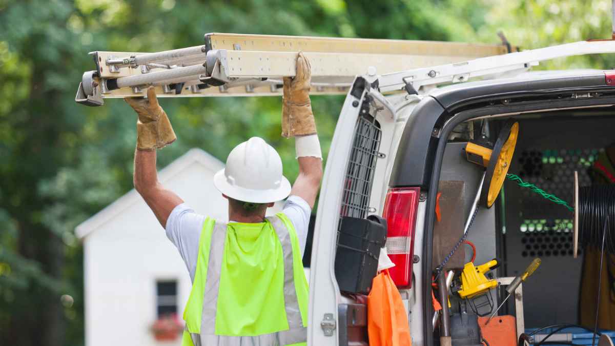Trabajador instalador cargando una escalera en una furgoneta de trabajo durante su desplazamiento laboral