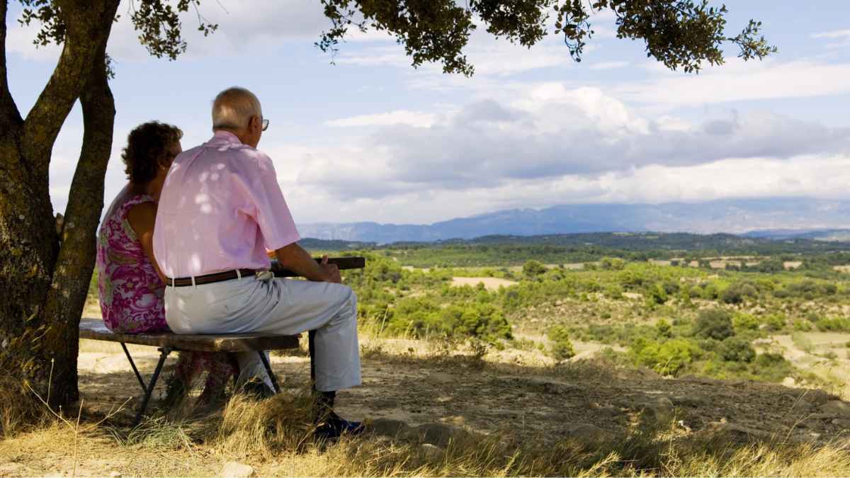 Personas mayores sentadas en un banco contemplando un paisaje natural