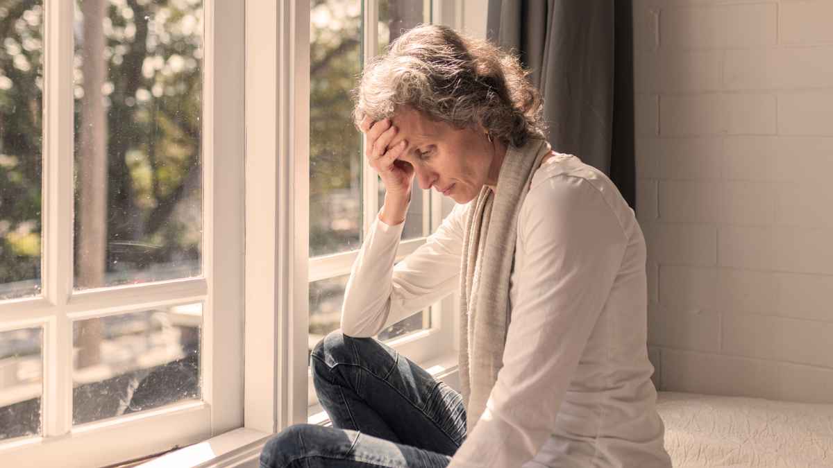 Mujer preocupada sentada junto a una ventana ante la posible retirada de la pensión de viudedad