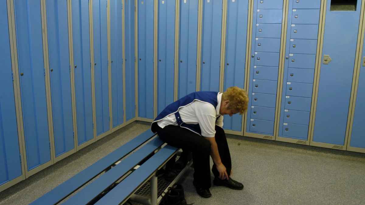 Trabajador sentado en un vestuario laboral mientras se cambia antes de iniciar su jornada