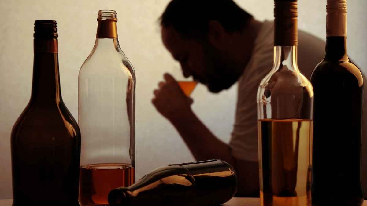 Hombre con problemas de alcoholismo junto a varias botellas sobre la mesa