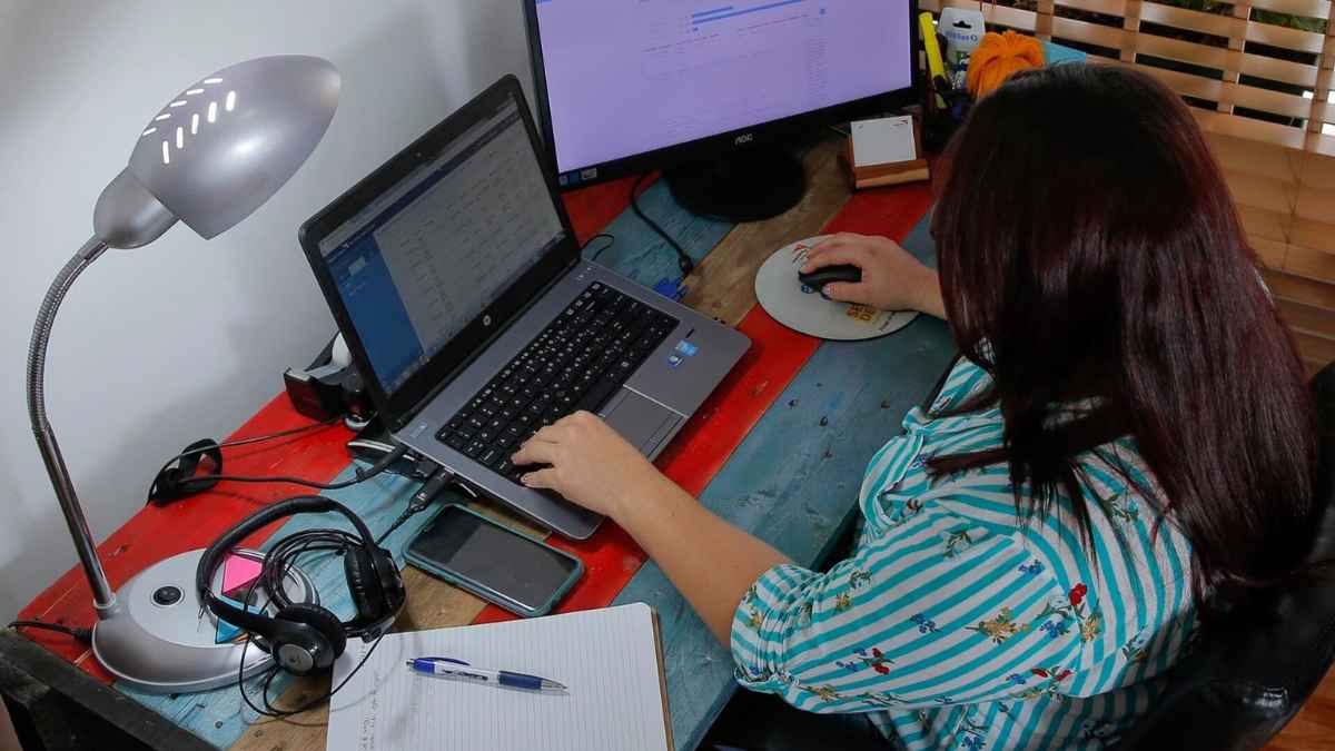 Teletrabajadora utilizando ordenador portátil y monitor en su puesto de trabajo en casa