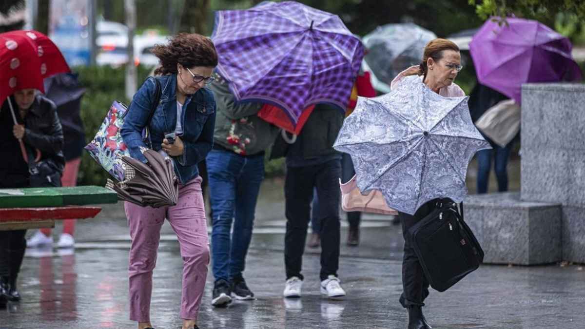 Trabajadores caminando bajo la lluvia intensa con paraguas durante un episodio de mal tiempo