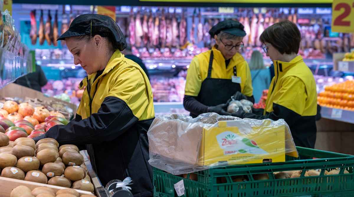 Empleados de AhorraMas trabajando como reponedores en sección de frutería de supermercado