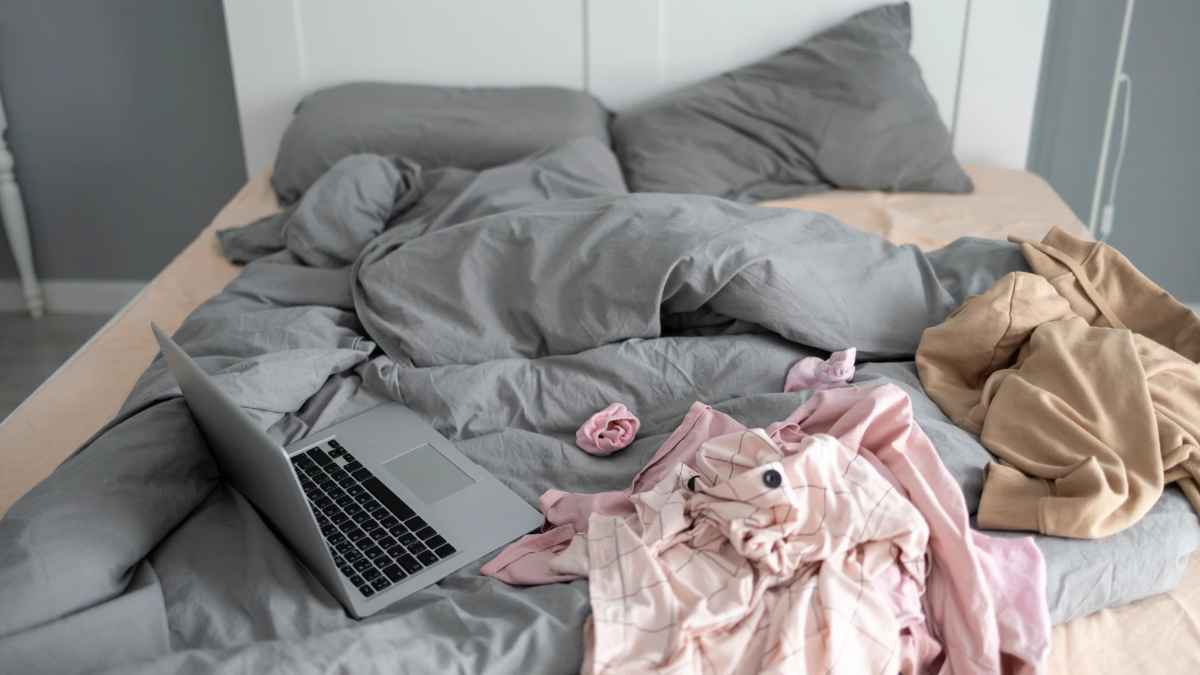 Cama sin hacer por la mañana con portátil y ropa desordenada, asociada a creatividad y habilidades laborales