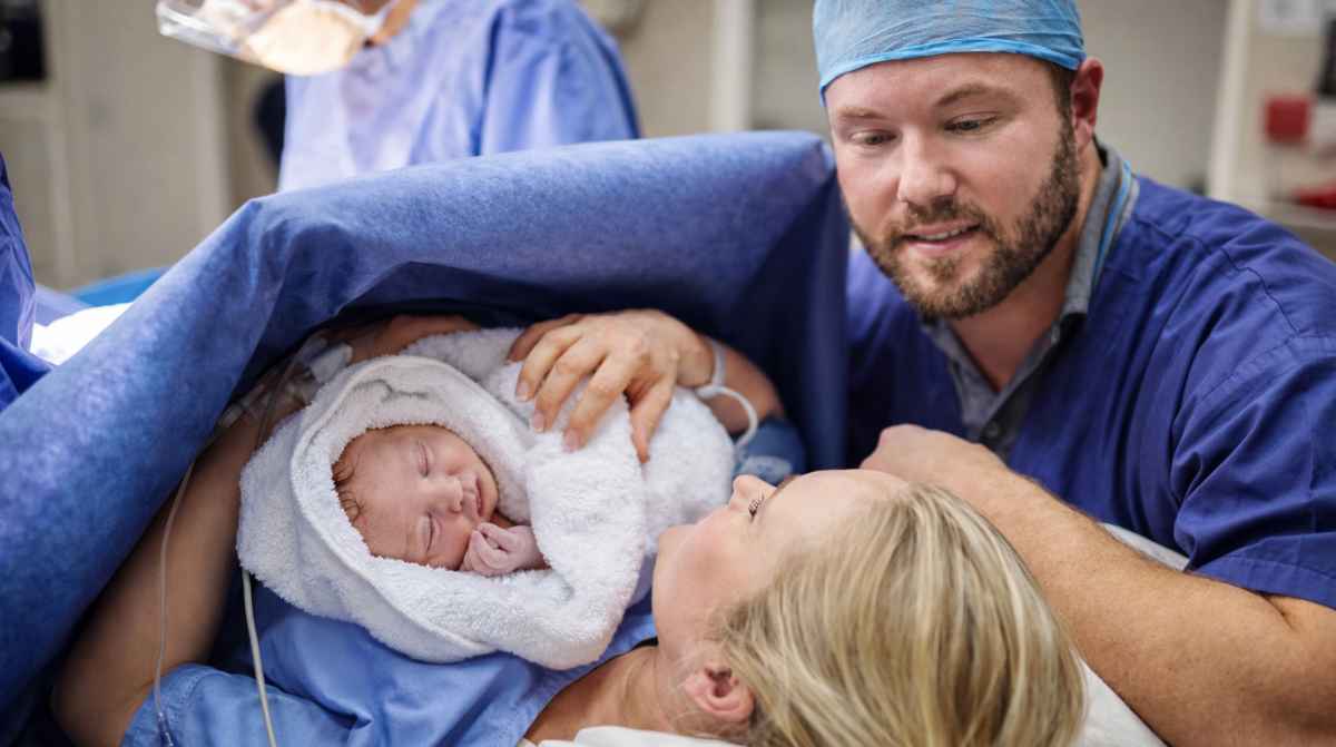 Madre y padre con su bebé recién nacido en el hospital tras el parto, imagen relacionada con la prestación por nacimiento 2026 de la Seguridad Social