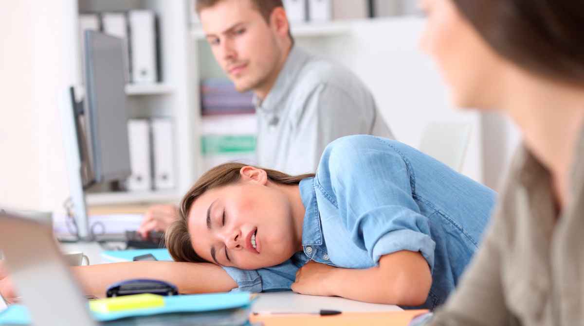 Trabajadora en la oficina llegando tarde al trabajo mientras sus compañeros observan, ejemplo de tolerancia empresarial y despido