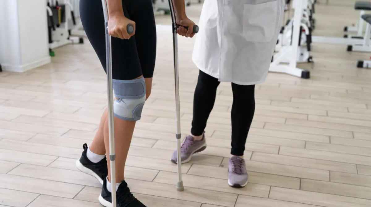 Trabajadora con rodillera y muletas durante una baja por incapacidad temporal tras recaída médica