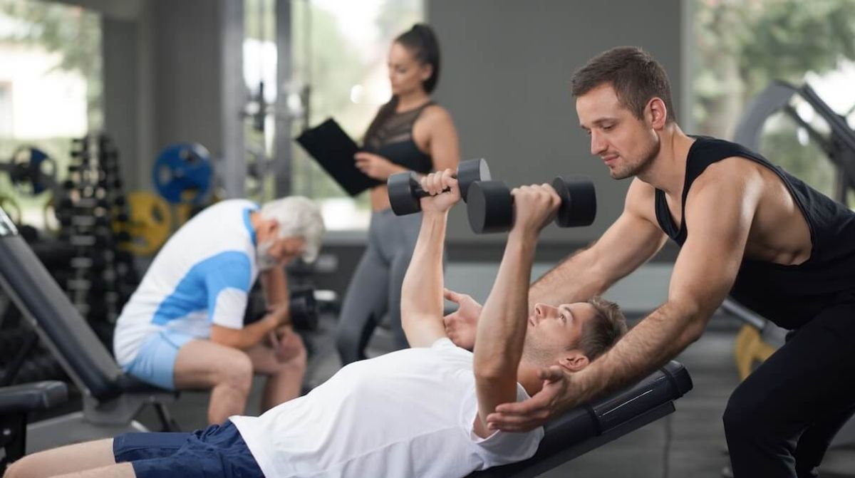 Entrenador personal ayudando a alumno en gimnasio durante entrenamiento de fitness Davante