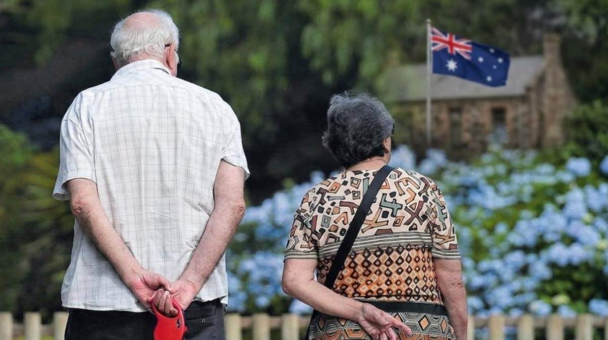 Personas mayores caminando con bandera de Australia al fondo, representando el sistema de pensiones australiano