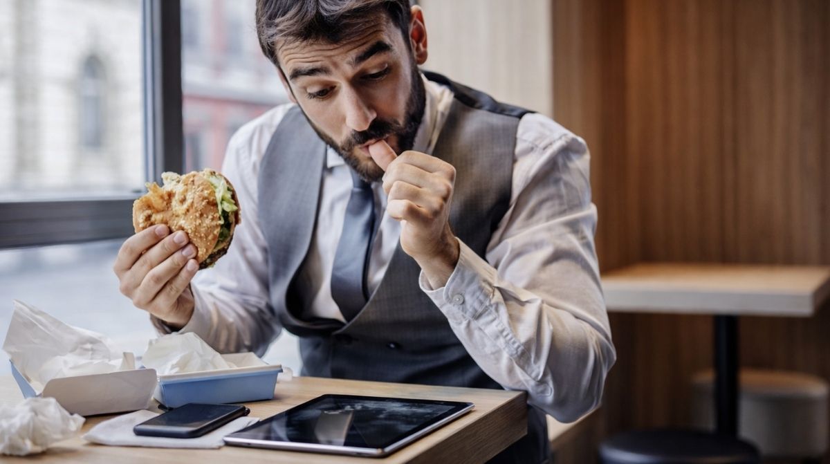 Trabajador comiendo durante su pausa mientras revisa el móvil y la tablet en horario laboral