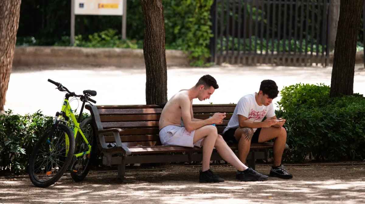Jóvenes sentados en un banco con el móvil, imagen ilustrativa sobre la retirada de pensión a ninis de 20 años por no estudiar ni trabajar
