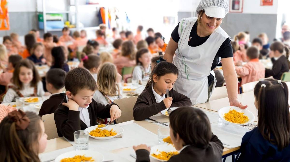 Monitora de comedor escolar atendiendo a niños durante la comida en un colegio