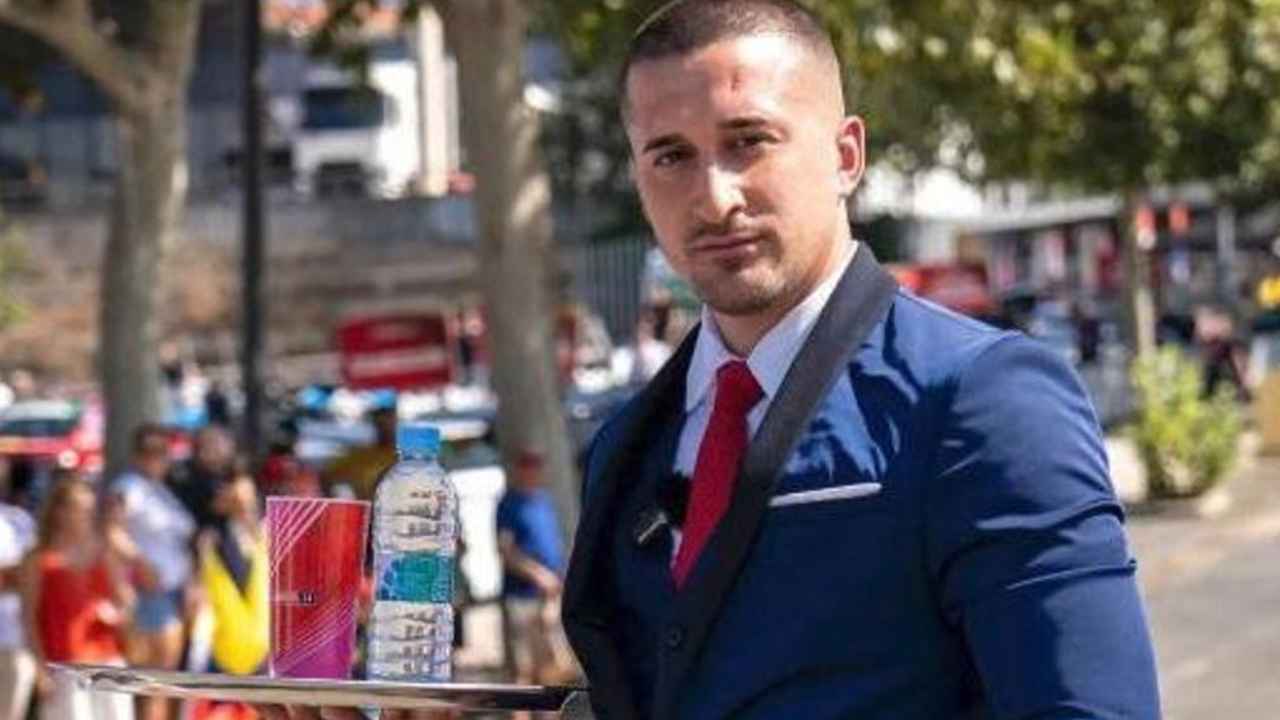 Cristian Ventura sostiene una bandeja vestido de camarero junto a una playa de Mallorca