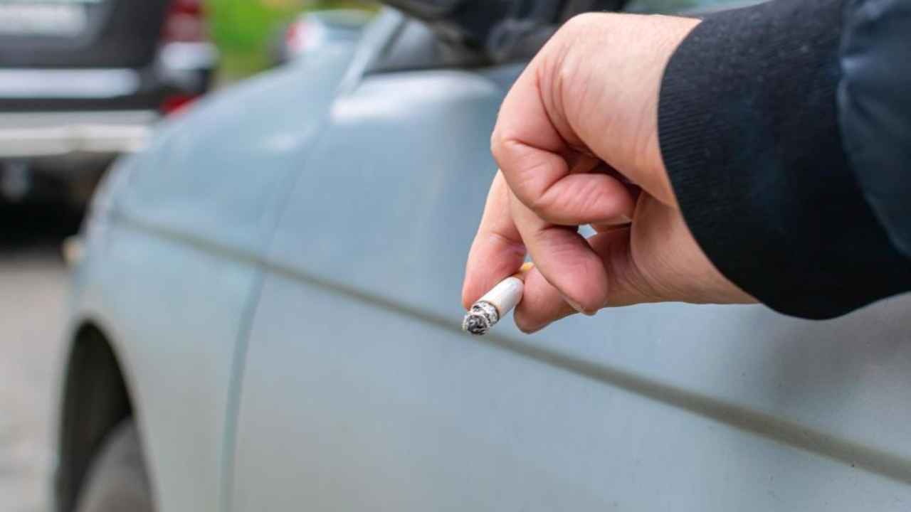 Conductor arroja una colilla por la ventanilla de un coche en carretera.