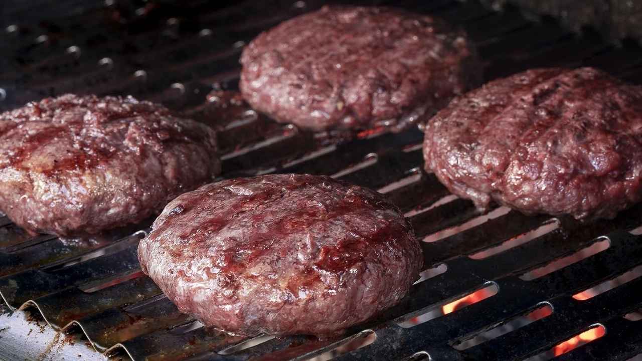 Cuatro hamburguesas de carne cocinándose sobre una parrilla